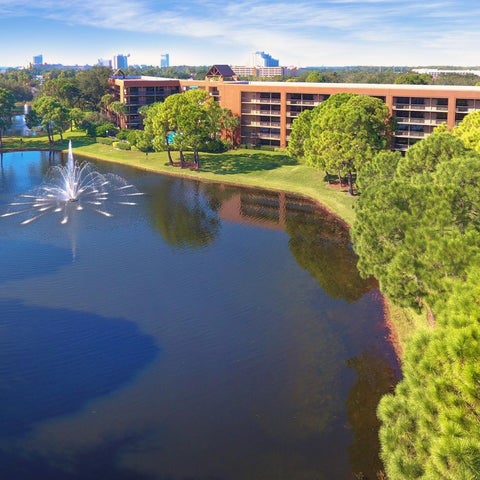 A large hotel complex with a pond featuring a fountain and lush greenery surrounds the building.