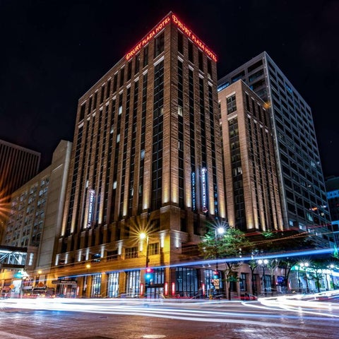 A tall building with illuminated windows and a distinctive rooftop design stands amidst other urban structures at night.