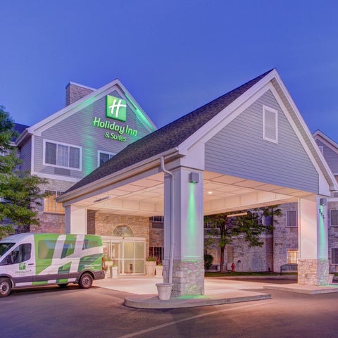 A Holiday Inn & Suites building with a covered entrance and a shuttle van parked in front, illuminated by green lighting.