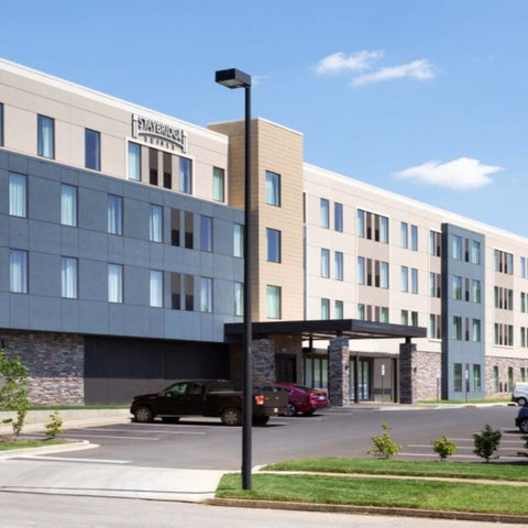 A modern hotel building with a gray and beige facade, a parking lot, and landscaping in front.