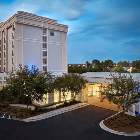 A multi-story Holiday Inn hotel building with a modern facade, surrounded by landscaping and a covered entryway.