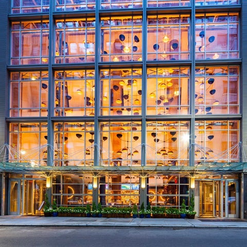 A modern building facade features a large glass curtain wall with visible interior lighting and a covered entrance.