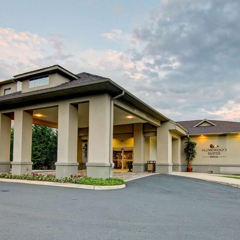 A beige and gray HomeWood Suites building with a covered entrance and American flag visible in front of it.