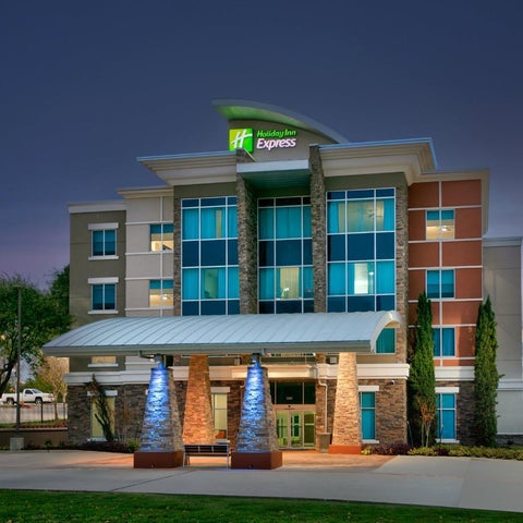 A modern Holiday Inn Express building with a multi-story facade, entranceway, and landscaping at dusk.