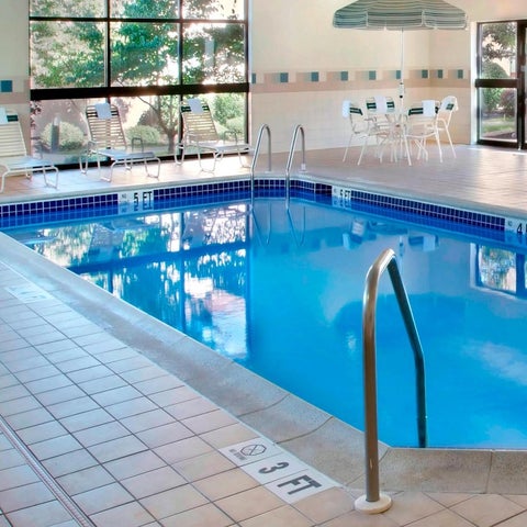 An indoor pool with tiled decking and lounge chairs is visible through a large window.