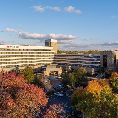 A large Marriott hotel complex with multiple buildings and parking areas is surrounded by trees with autumn foliage.