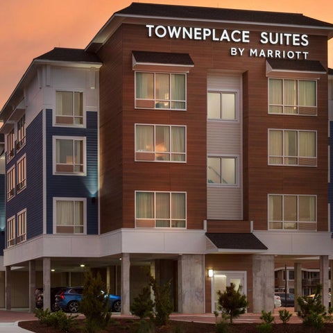 A multi-story TownePlace Suites by Marriott hotel building with a modern facade and parking area at dusk.