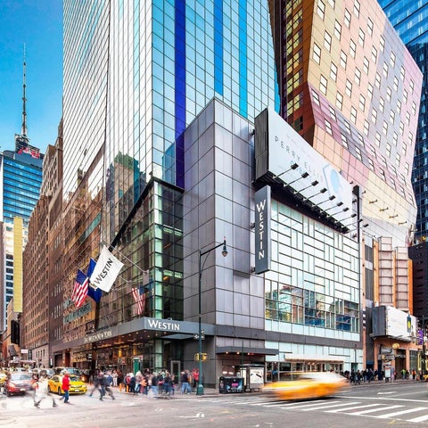 A wide view of the Westin New York at Times Square, showcasing its facade and bustling street-level activity with surrounding buildings.