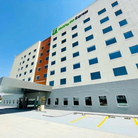A modern Holiday Inn Express building features a light gray facade, a covered entrance, and a parking area with yellow-lined spaces.