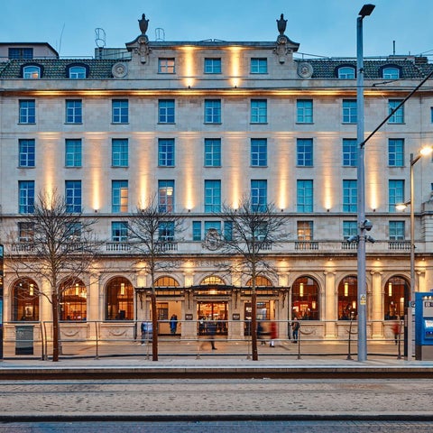 A grand, illuminated building facade with a prominent entrance and street-level views of a city.