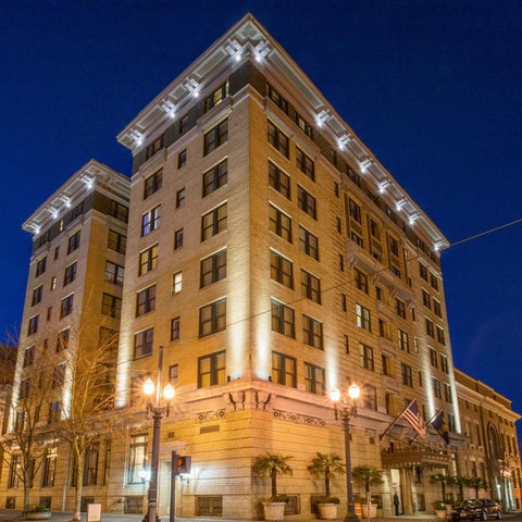 A large, illuminated hotel building stands against a dark blue sky with streetlights and landscaping visible in the foreground.