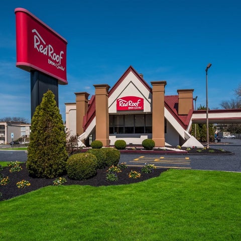 A Red Roof Inn & Suites building features a red and white sign, a covered driveway, and manicured landscaping.