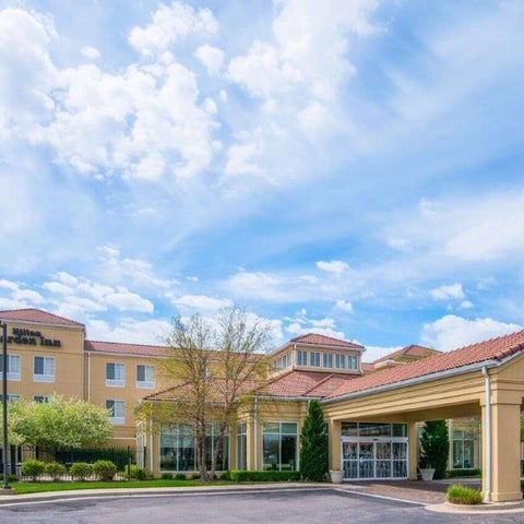 A multi-story hotel with a red tile roof and a covered entrance sits on a green lawn under a partly cloudy sky.