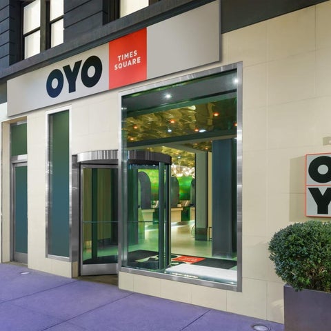 The entrance of the OYO Times Square hotel features a glass facade, signage, and a potted plant on the sidewalk.