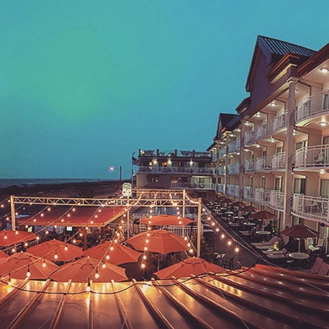 A multi-story hotel with outdoor seating and patio umbrellas is illuminated against a twilight sky.