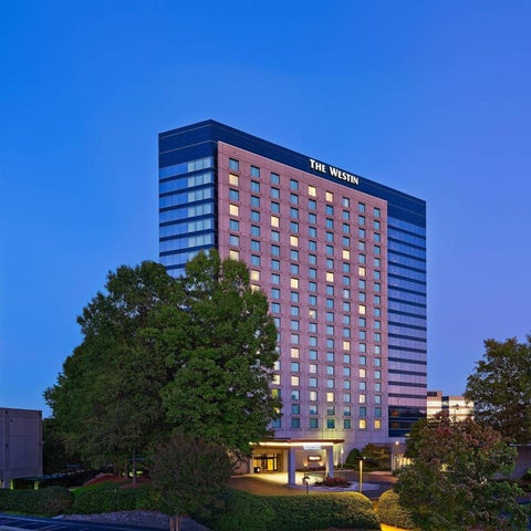 The Westin hotel building is illuminated against a twilight sky, with trees and other buildings visible in the foreground.