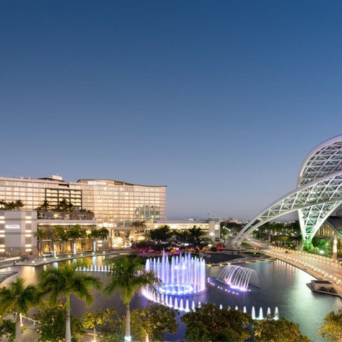 A large resort complex with modern architecture, fountains, and lush landscaping is illuminated against a twilight sky.
