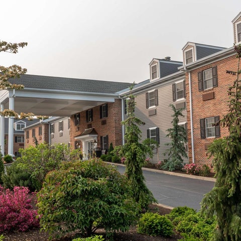 A brick building with a covered entrance and manicured landscaping is seen on a slightly overcast day.