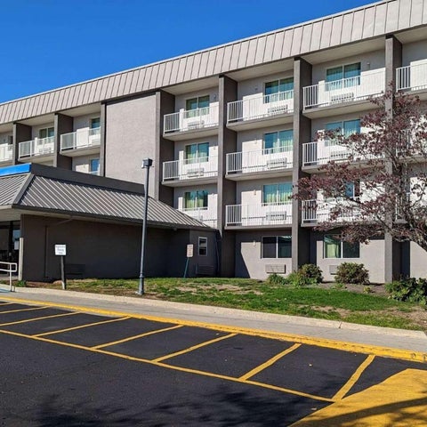 A multi-story hotel building with a covered entrance and parking lot featuring marked spaces and landscaping.