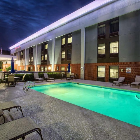 An outdoor pool with lounge chairs and a patio area is situated in front of a hotel building at dusk.