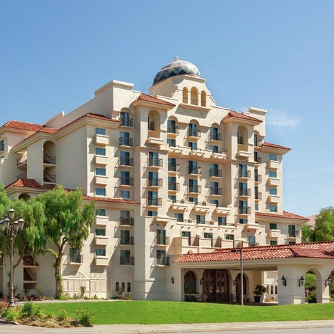 A large, ornate hotel building with a domed tower and palm trees stands against a clear blue sky.
