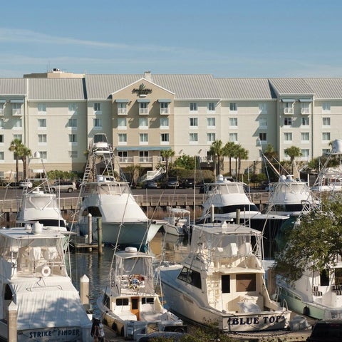 A large, white hotel building with multiple floors overlooks a marina filled with several docked boats and palm trees.