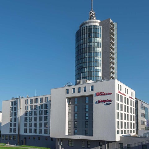 A Hampton by Hilton hotel complex features a distinctive cylindrical tower and a lower, rectangular building with a modern facade.