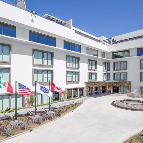 A modern, white building with flags and a circular driveway featuring landscaping and a stone entrance.