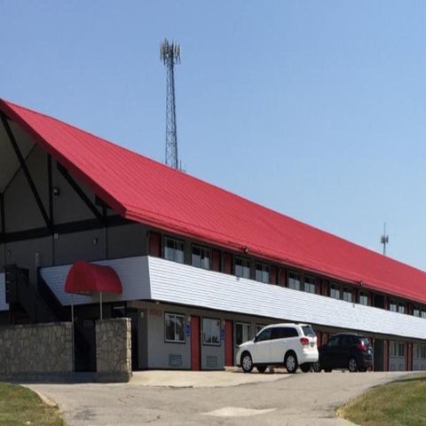 An economy inn motel with a red roof and signage is visible against a bright blue sky with a school bus in the background.