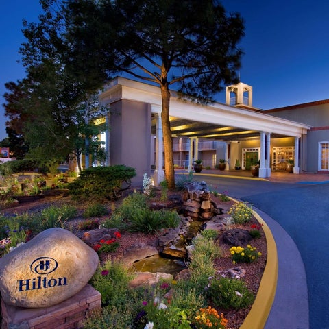 A Hilton hotel entrance features a landscaped garden, a covered walkway, and a prominent Hilton sign.