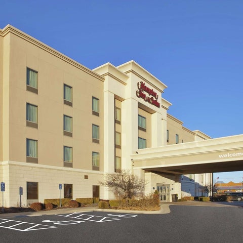 A large, multi-story Sheraton hotel building with a covered entrance and parking lot visible in front.