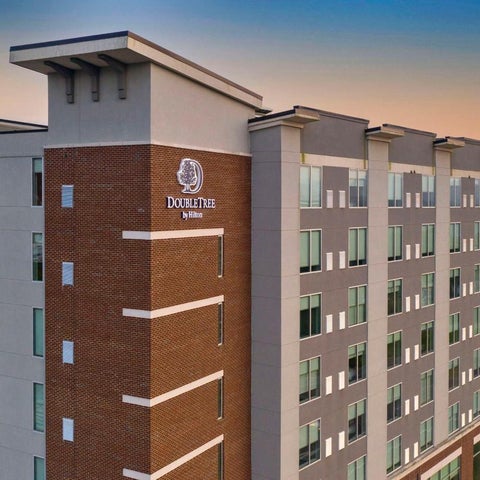 A multi-story DoubleTree hotel building with a brick and gray facade is shown against a sunset sky.