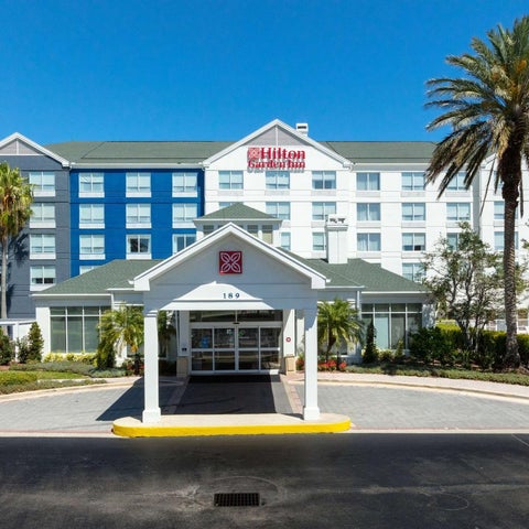 A Hilton Garden Inn building facade with a covered entrance, palm trees, and a blue and white striped design.