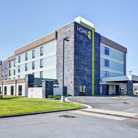 A modern Home2 Suites by Hilton hotel building with a gray and white facade and a covered entrance.