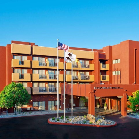 A red and tan hotel building with American and hotel flags displayed prominently in front of the entrance.