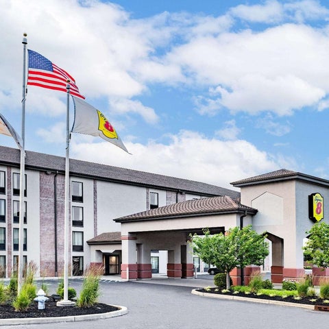 A modern hotel building with a covered entrance, flags, and landscaping under a partly cloudy sky.