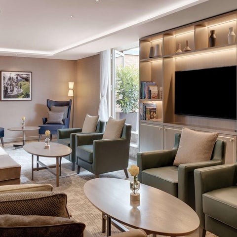 A well-lit lounge area features plush seating, a coffee table, and a large television within a built-in shelving unit.