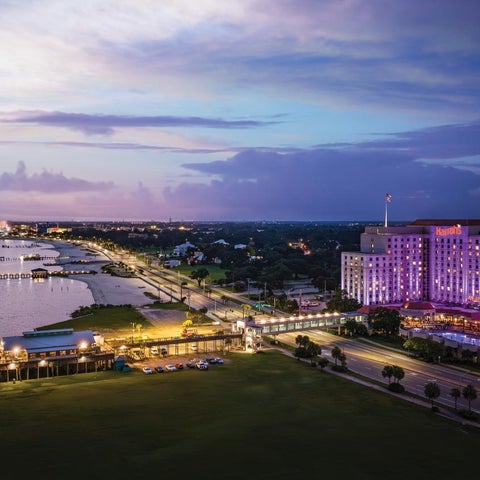An aerial view showcases a coastal city at dusk, featuring a brightly lit hotel and waterfront structures.
