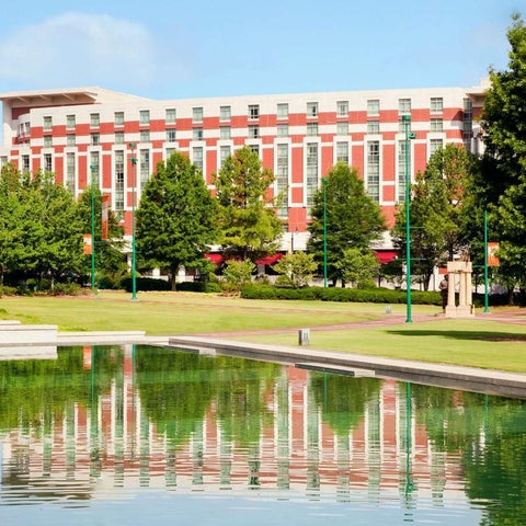 A large, red and white building with a reflecting pool and lush greenery in the foreground.