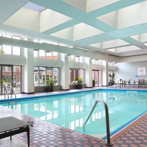 An indoor pool with a tiled deck, lounge chairs, and large windows overlooking an outdoor area.