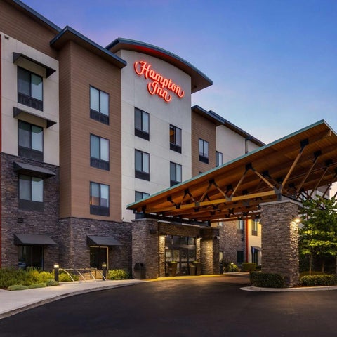 A Hampton Inn hotel building with a covered entrance and landscaping is shown at dusk.