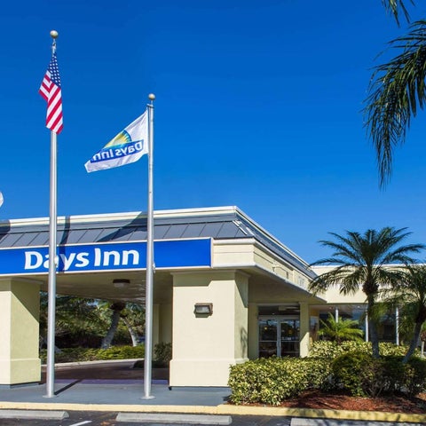 A Days Inn hotel facade is shown with flags, palm trees, and a low-rise building with a covered entrance.