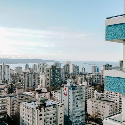 A cityscape view showcases a dense urban area with numerous high-rise buildings and a distant body of water under a cloudy sky.