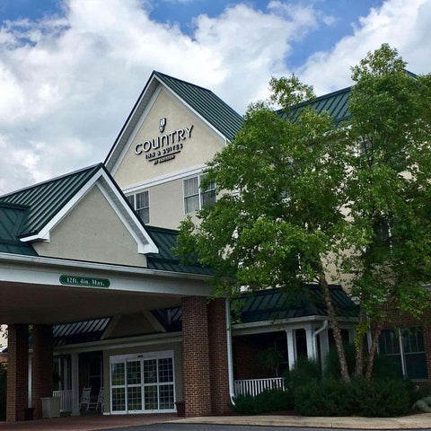 A Country Inn & Suites hotel building is shown with a brick facade, green roof, and a tree in the foreground.