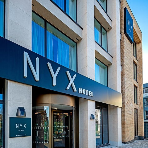 The exterior of the NYX Hotel features a modern facade with a prominent sign and revolving door entrance.