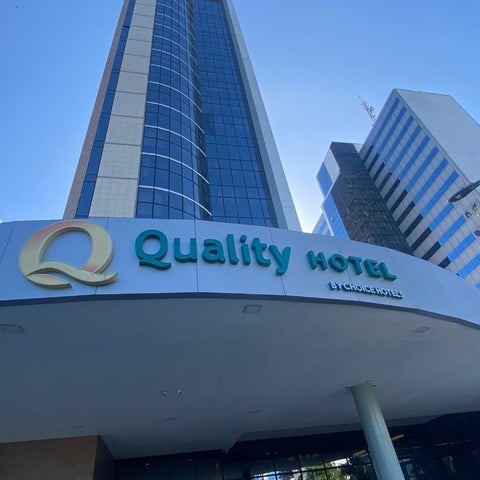 The Quality Hotel building facade is shown with its prominent signage and entrance area against a clear blue sky.