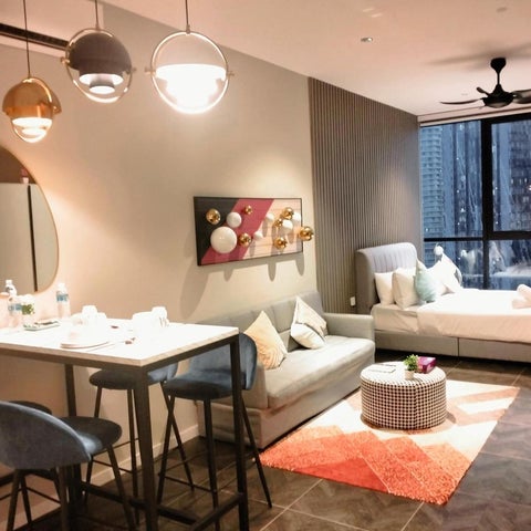 A modern studio apartment features a dining set, sofa, and decorative elements against a backdrop of a large window.