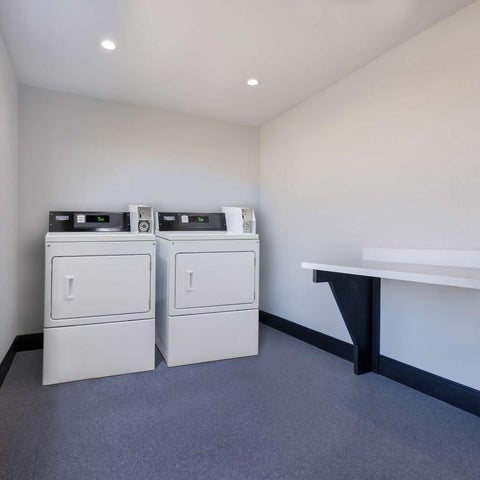 A laundry room features two white dryers and a built-in countertop against a gray-toned wall with a window.