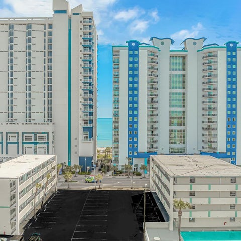 A view of several tall, modern beachfront buildings with blue and white facades and adjacent parking structures.