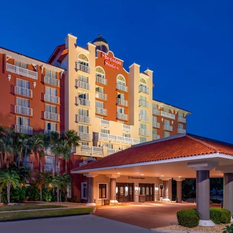 A brightly lit Hilton hotel building with a red-tiled roof and palm trees in front of a blue dusk sky.